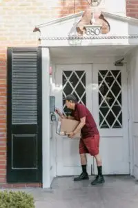 A courier in uniform delivers a package at a residential entrance, ringing the doorbell.